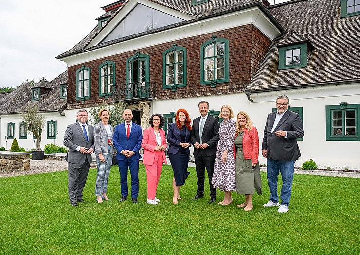 © NLK Burchhart Personen stehen auf Wiese vor Haus nebeneinander