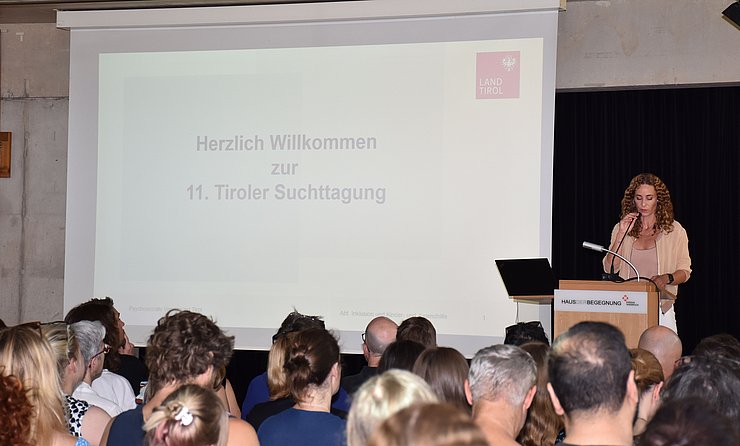 LRin Pawlata steht auf Bühne am Rednerpult, Saal mit Personen auf Stühlen von hinten fotografiert