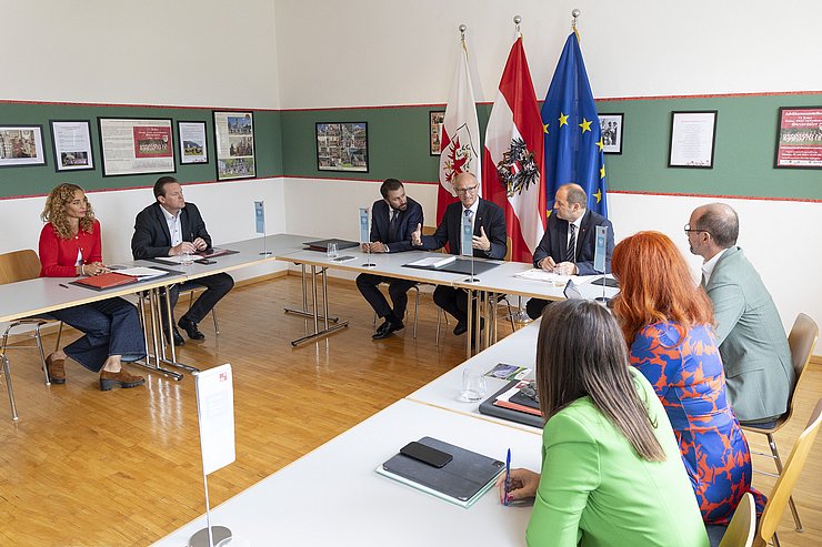 Die Mitglieder der Landesregierung sitzen in einer U-Formation um einen Tisch herum und diskutieren über bestimmte Themen.