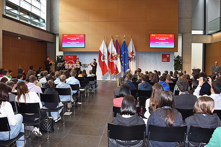 © Land Tirol/Dorfmann Raum mit SchülerInnen, die sitzen, vorne Fahnen und Bildschirme