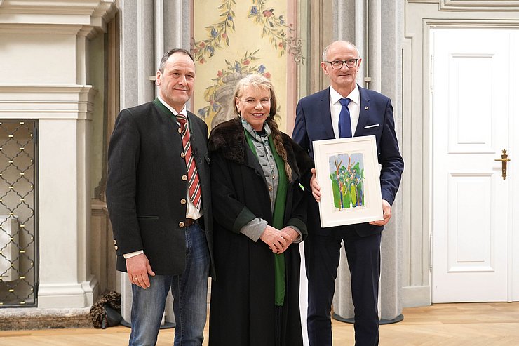 Drei Personen schauen in die Kamera und halten ein Bild in der Hand.