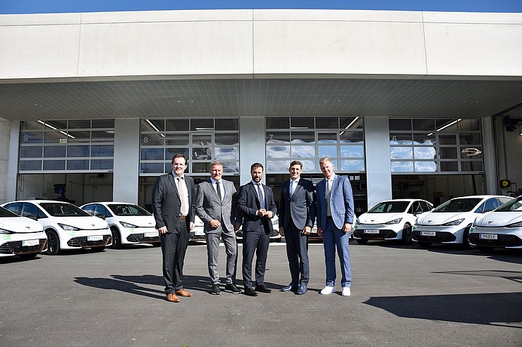 © Land Tirol/Pölzl Gruppenfoto; im Hintergrund stehen mehrere weiße E-Autos aufgereiht