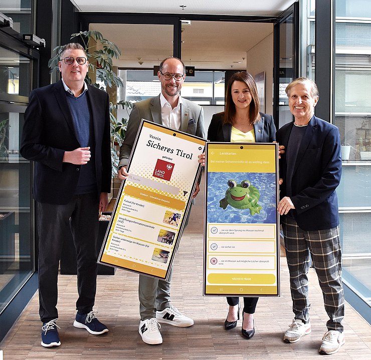 © Land Tirol/Hörmann Gruppenfoto; Mair und Gerber halten große Tafeln mit Mockups der App