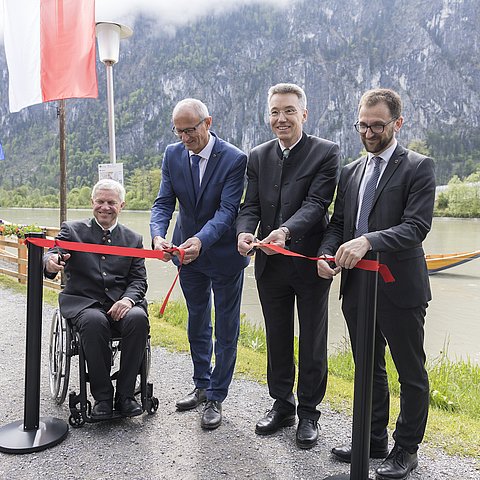 Gruber (im Rollstuhl), Mattle, Lederer und Kolland hinter einem roten Band mit Scheren in der Hand und schneiden das Band durch; im Hintergrund der Inn; im linken Bildrand Fahnen