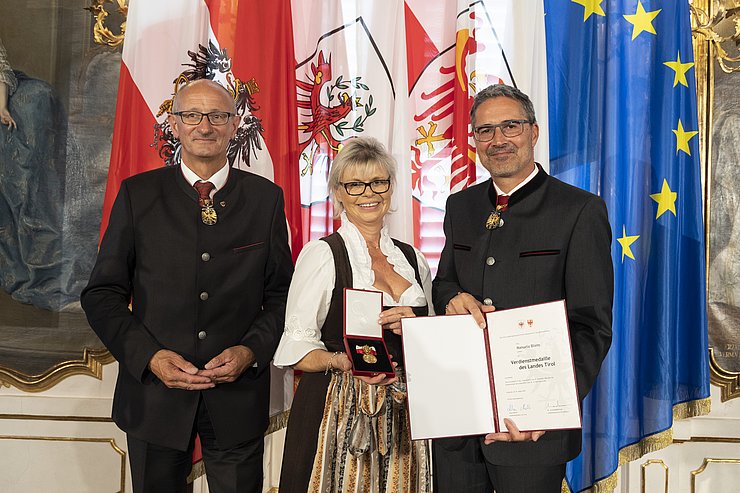 © Land Tirol/Die Fotografen links LH Mattle, in der Mitte Frau Bliem und rechts LH Kompatscher, halten Medaille und Verdiensturkunde