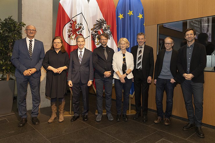 © Land Tirol/Die Fotografen Mehrere Personen stehen im großen Landhaussaal vor drei Fahnen.