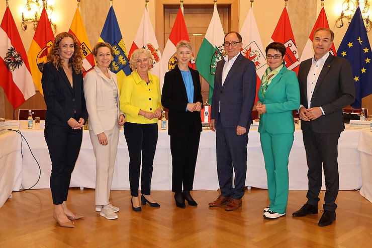 Personen nebeneinanderstehend, vor Fahnen