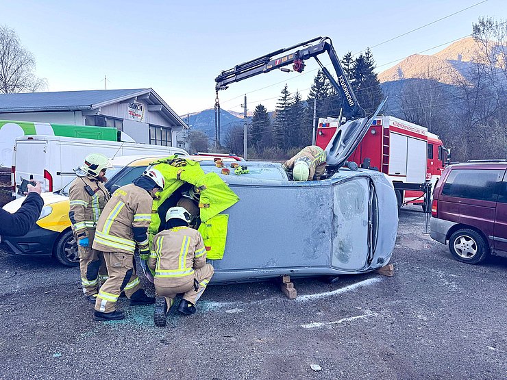 Mehrere Feuerwehrleute dringen über das Rückfenster in ein seitlich liegendes Auto ein. 
