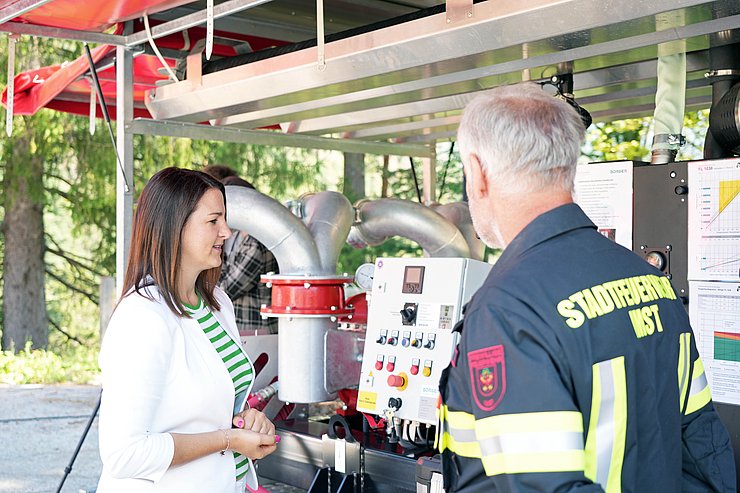 © Land Tirol/Hörmann LRin Mair mit Feuerwehrmann vor Grußpumpe redend