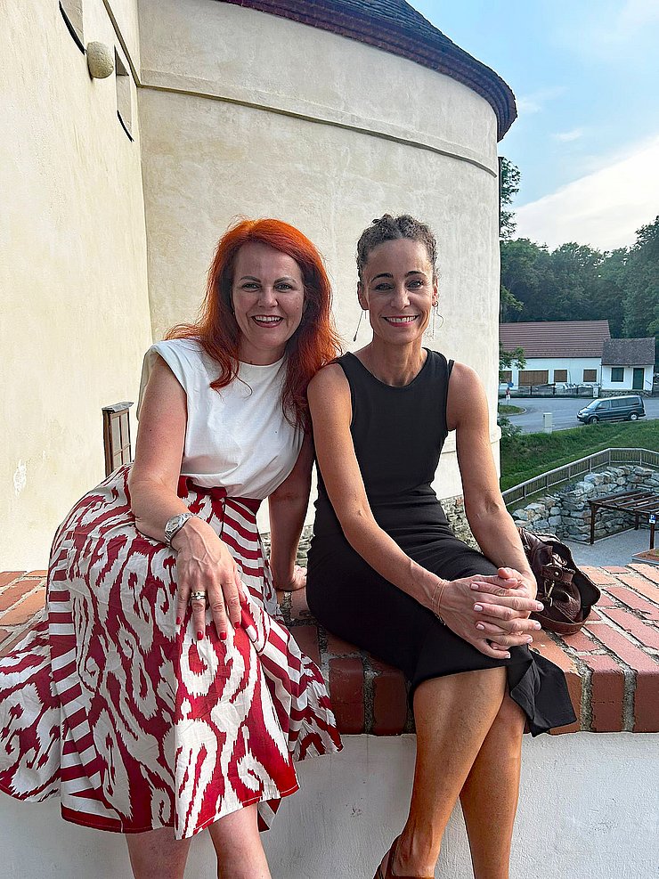 LRinnen sitzen auf Mauer, dahinter ist ein Teil des Gebäudes und die Landschaft zu sehen