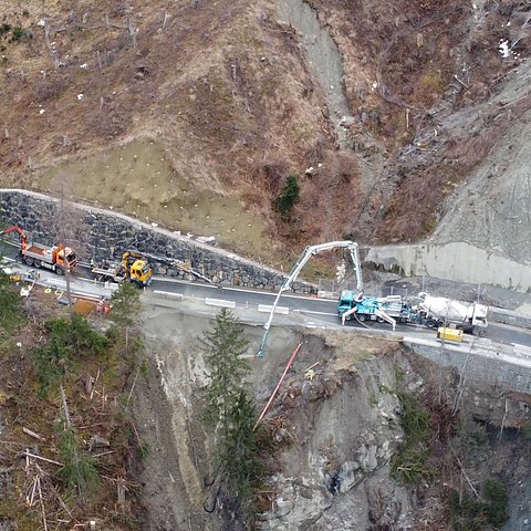 Vier LKWs arbeiten an einer Landstraße, da darunter ein Hang abgerutscht ist.
