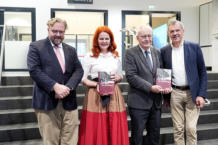 Vier Personen stehen auf einer Treppe, drei Männer und eine Frau.