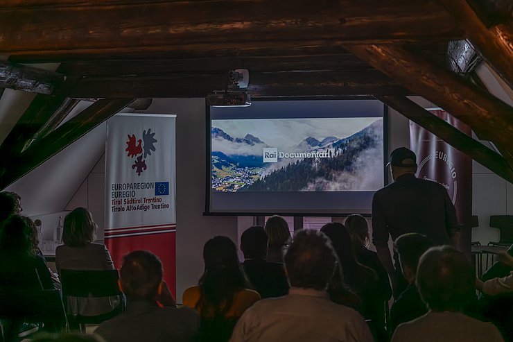 © LPA/Daniel von Johnston Mehrere Menschen sitzen in einem Saal und schauen auf eine Leinwand.
